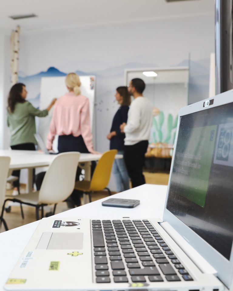 Vier Personen stehen vor einem Whiteboard, man sieht einen Laptop auf dem Tisch stehen, digitale Zertifikate sind zu sehen